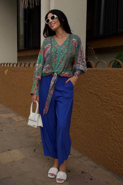 Woman wearing a colorful patterned blouse and  baggy royal blue pants.