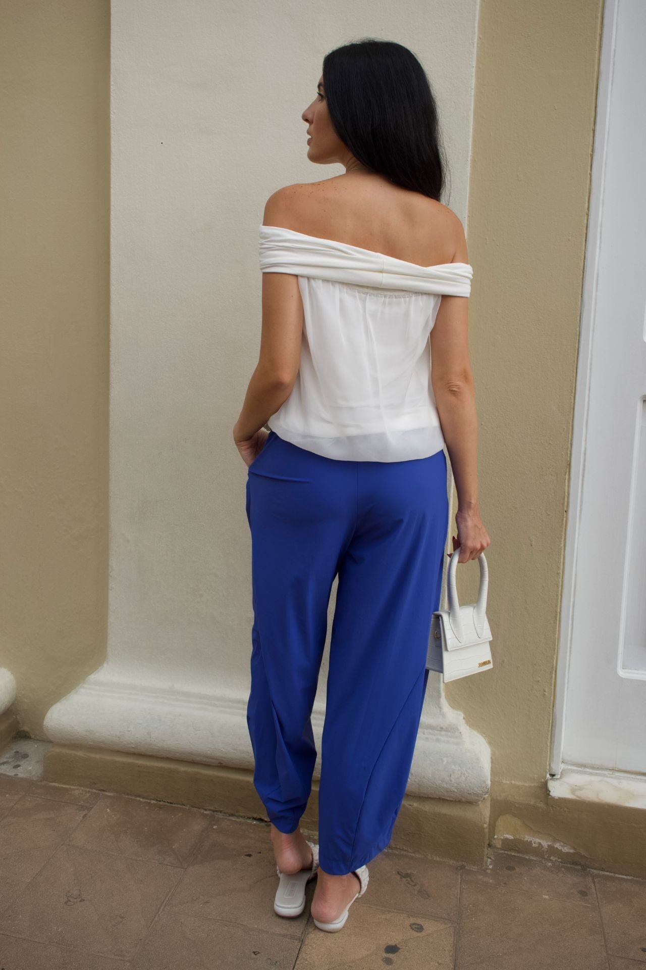 Back view of a woman wearing a white off-shoulder top and royal blue baggy pants 