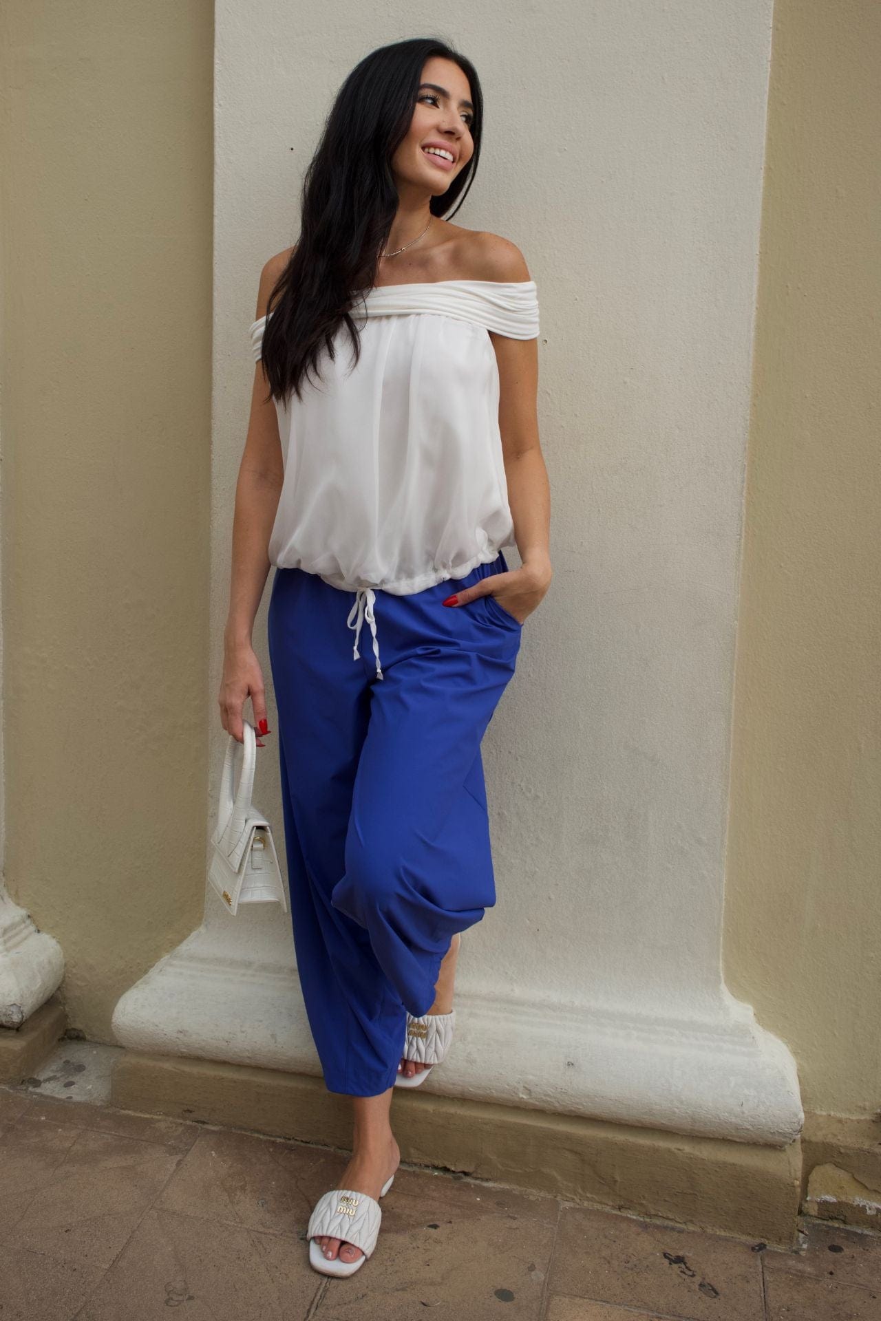 Front view of a woman wearing a white off-shoulder top and baggy royal blue pants.