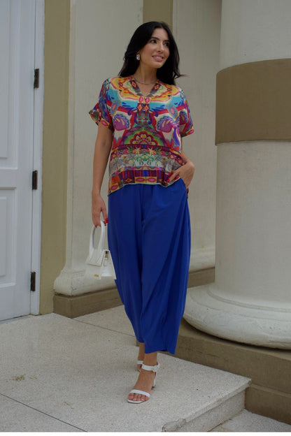 Front view of a woman wearing a colorful top and baggy royal blue pants. 