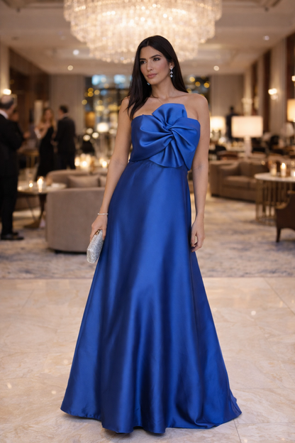Woman in a blue evening gown with a large bow in a luxurious interior setting.