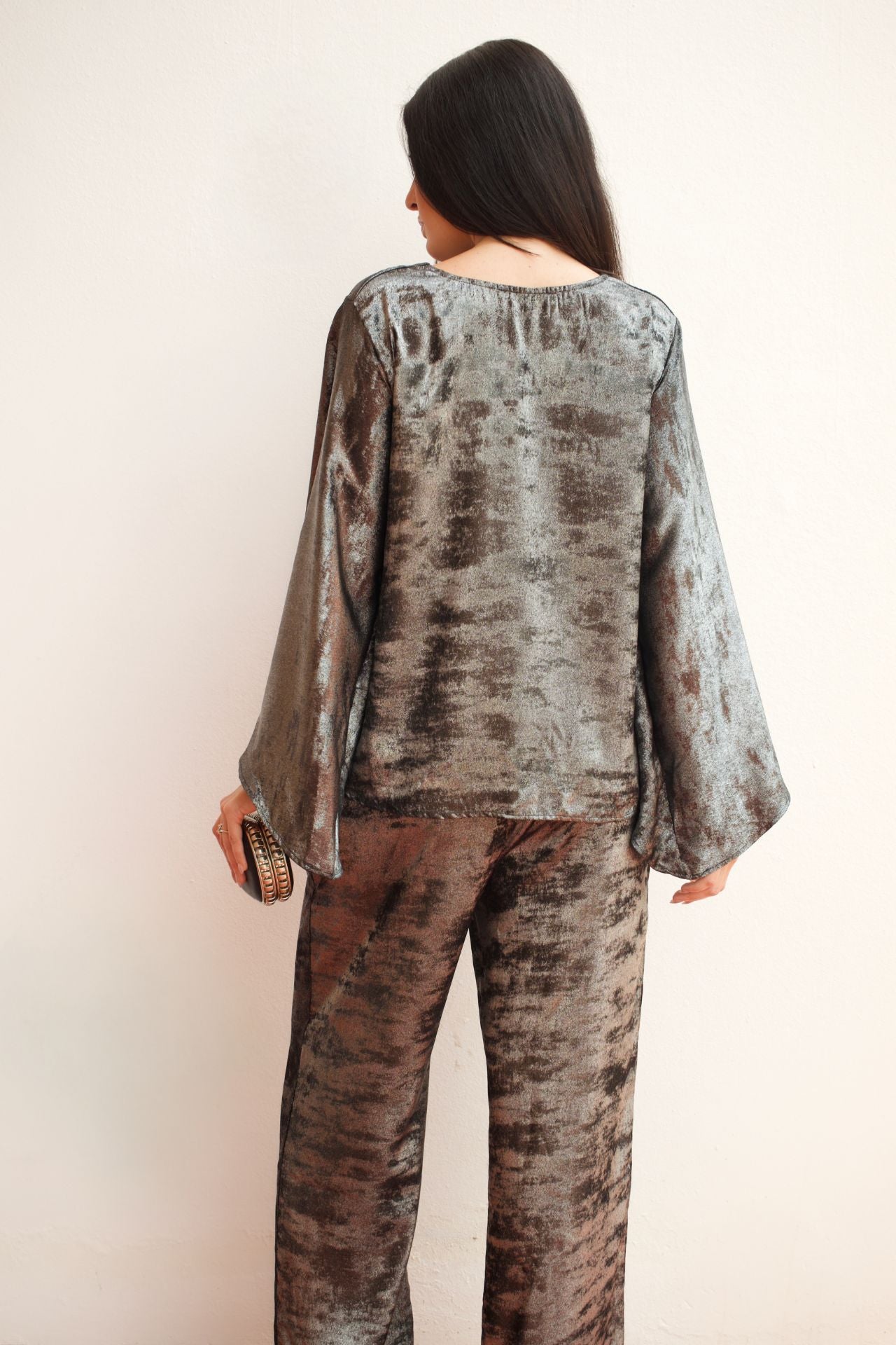 Model wearing a silver metallic two-piece pant set with a relaxed V-neck blouse, wide sleeves, and straight-leg pants styled for an elegant evening look.