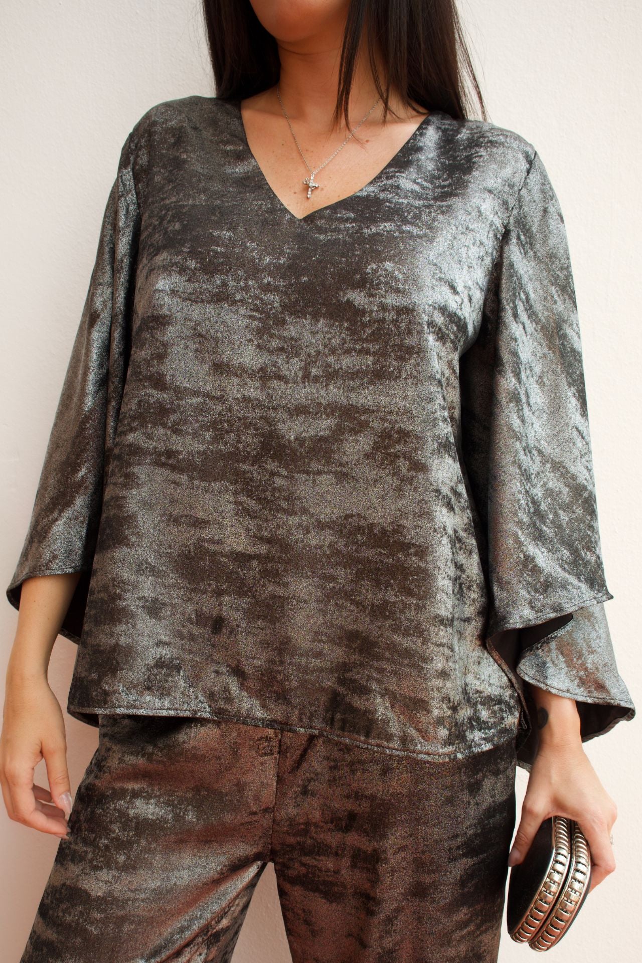 Model wearing a silver metallic two-piece pant set with a relaxed V-neck blouse, wide sleeves, and straight-leg pants styled for an elegant evening look.