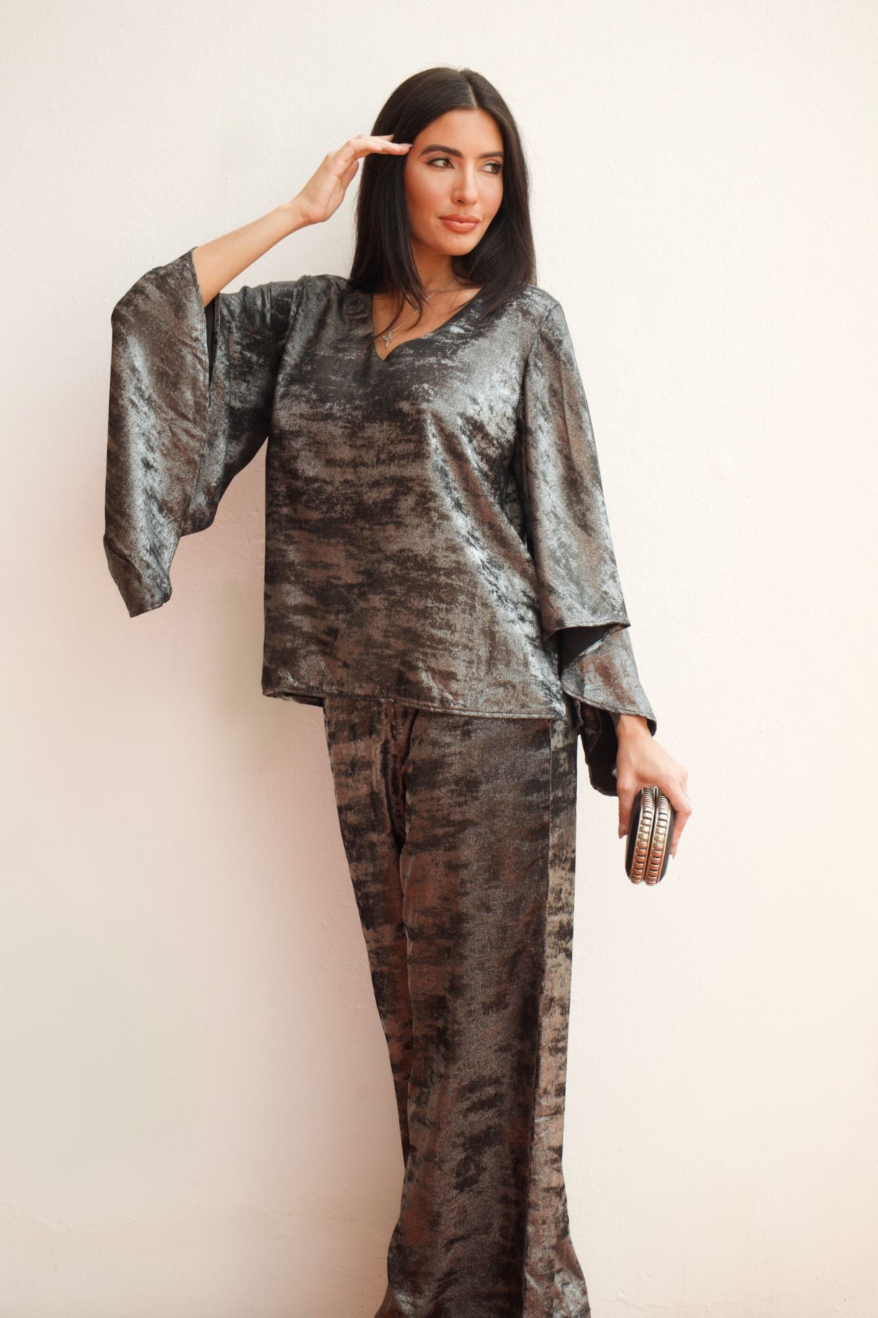 Model wearing a silver metallic two-piece pant set with a relaxed V-neck blouse, wide sleeves, and straight-leg pants styled for an elegant evening look.