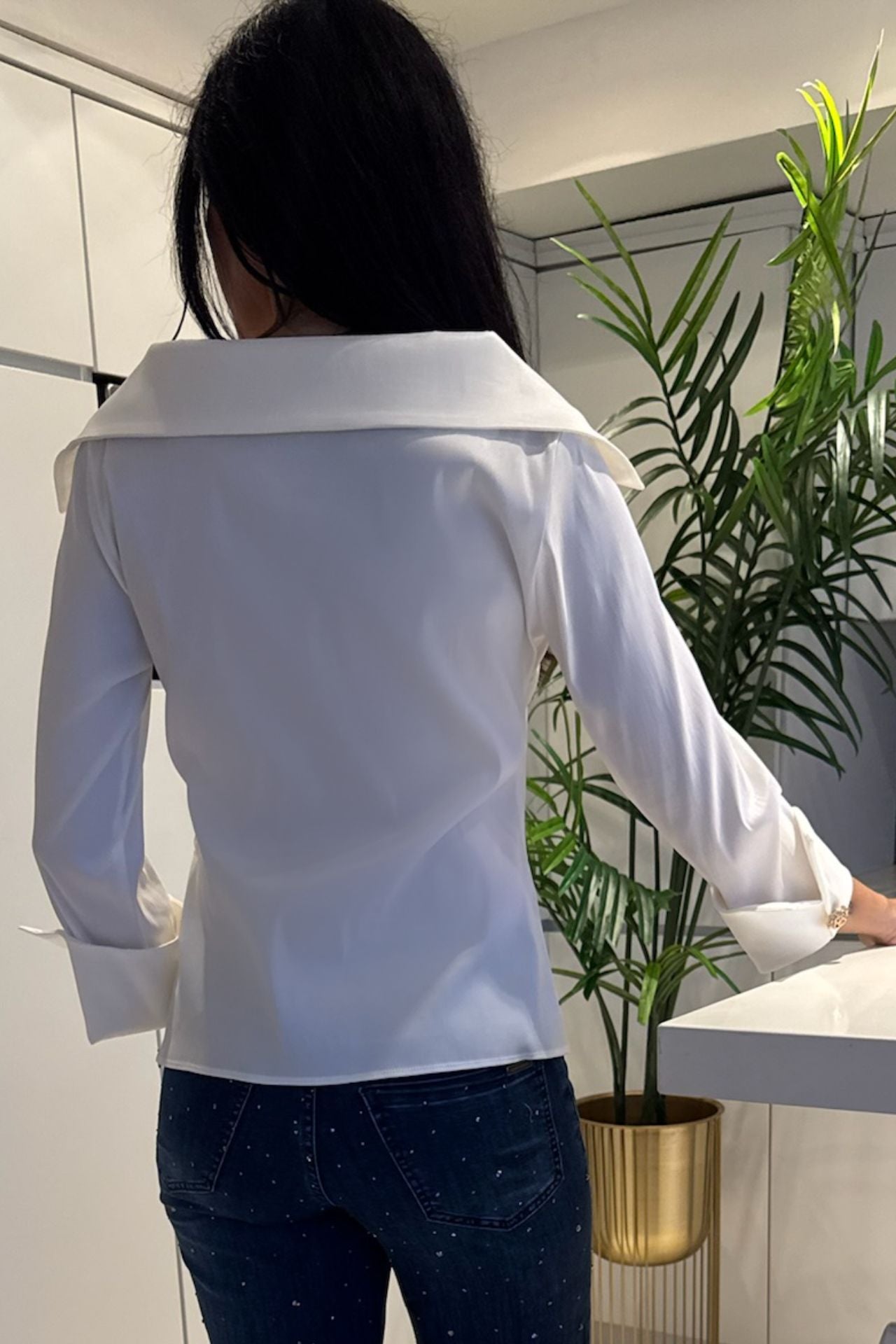 Back view of a woman wearing a white sailor collar blouse with wide statement cuffs paired with embellished denim.