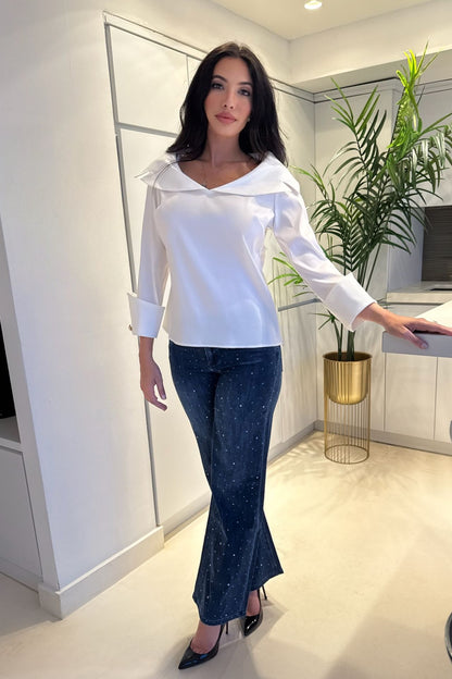 Woman wearing a white sailor collar blouse with wide statement cuffs paired with embellished denim.