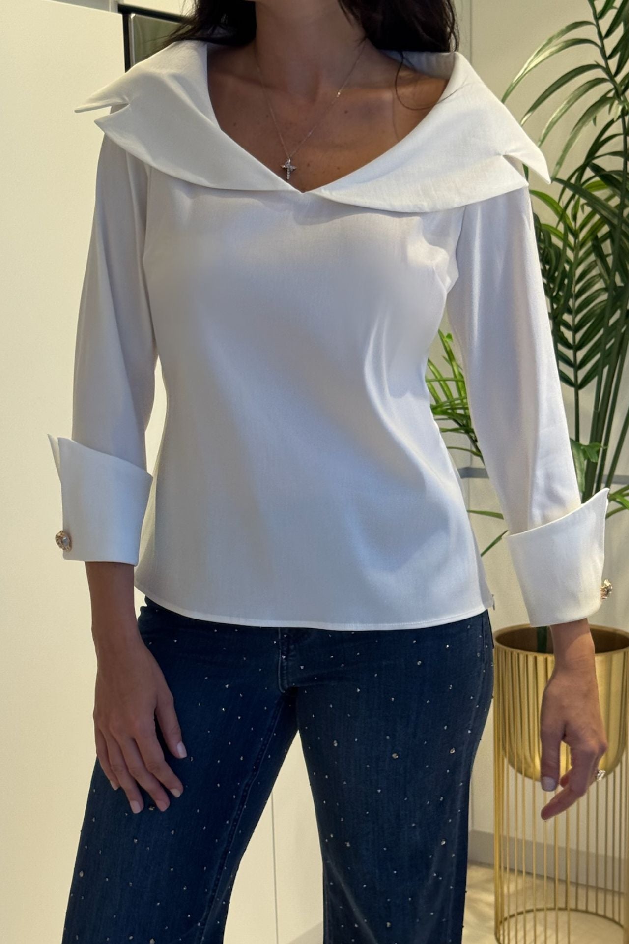 Woman wearing a white sailor collar blouse with wide statement cuffs paired with embellished denim.