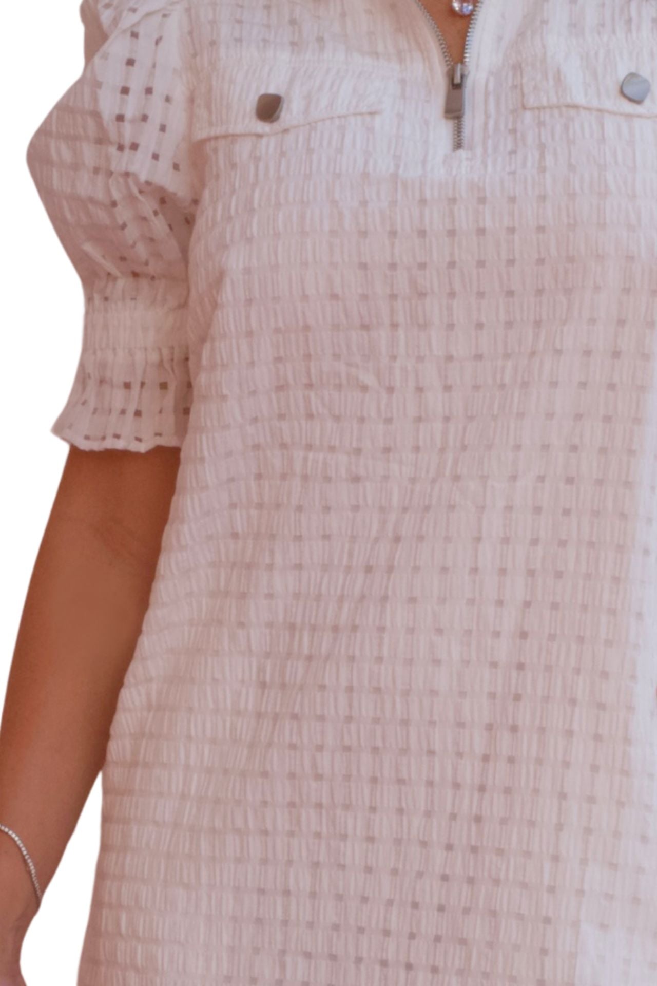 Woman wearing a white textured puff sleeve dress with front zip neckline and pockets.