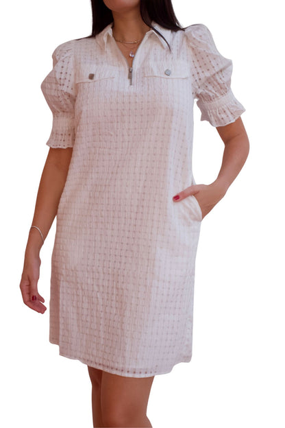Woman wearing a white textured puff sleeve dress with front zip neckline and pockets.