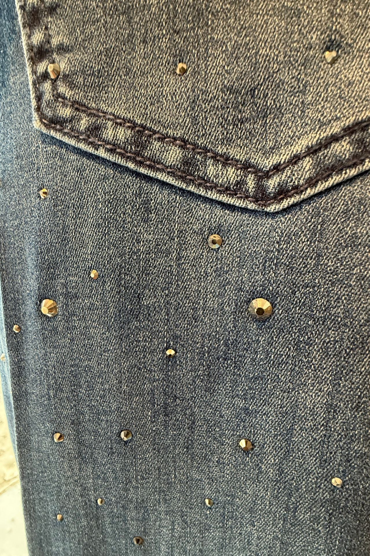 Close-up of wide-leg dark denim jeans with scattered crystal stud embellishments.